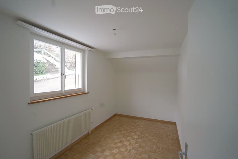 Empty room with wooden flooring, white walls, a window with a wooden sill, and a radiator below the window.