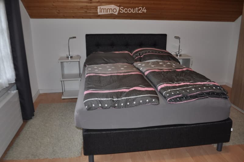 A neatly arranged bedroom with a double bed, nightstands, lamps, and a rug on the floor.