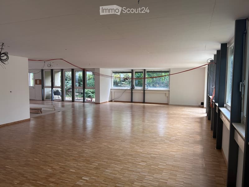 Empty room with wooden flooring, white walls, large windows, and visible electrical wires. No furniture or equipment present.