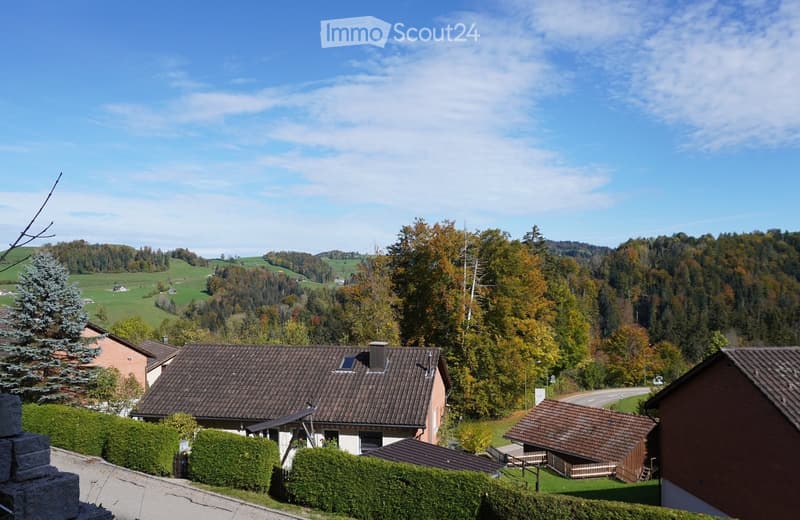 A two-story house with a brown tiled roof, surrounded by greenery and trees in a rural landscape.