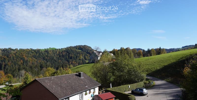 A picturesque view of a residential house nestled in a lush, green valley with rolling hills and scattered trees under a clear blue sky.