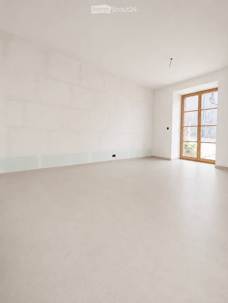 Empty room with white walls, light-colored tiled floor, and a large sliding glass door leading to an outdoor area.