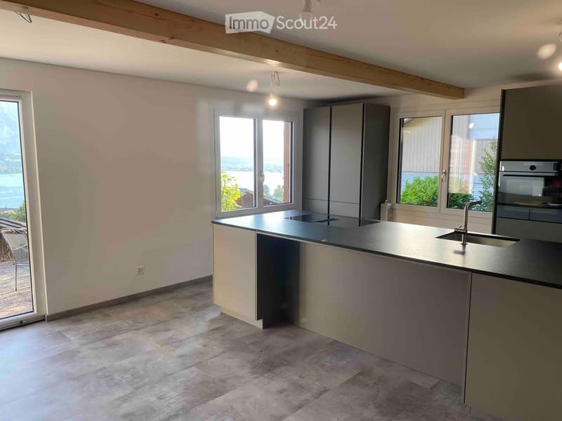 Modern kitchen with a central island, stainless steel sink, and built-in oven, large windows offering a scenic view.