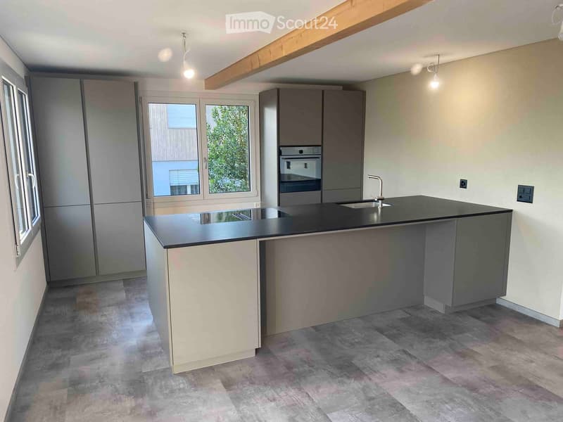 Modern kitchen with a central island, stainless steel appliances, and large windows.