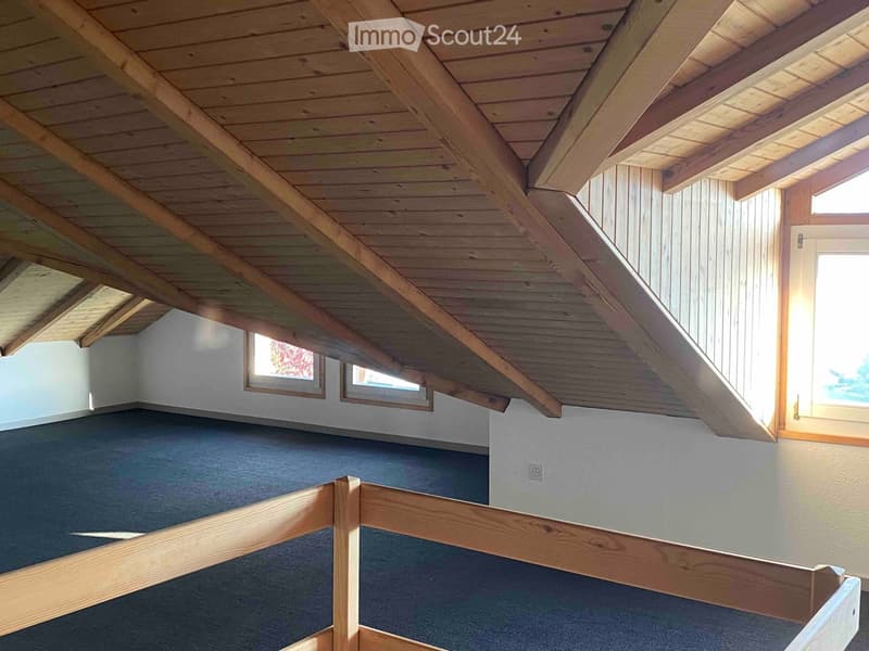 An empty attic space with exposed wooden beams, skylights, and a wooden railing overlooking the lower level.