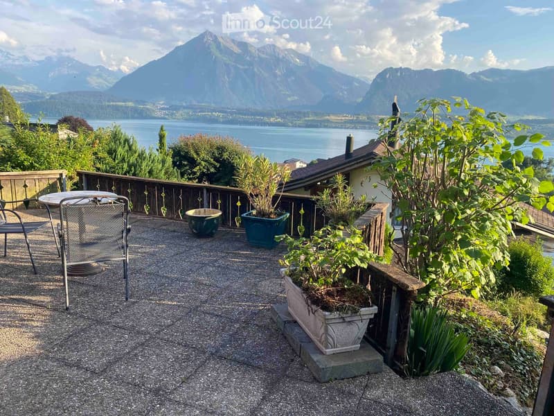 Balcony with a scenic mountain and lake view, featuring a table, chairs, and potted plants.