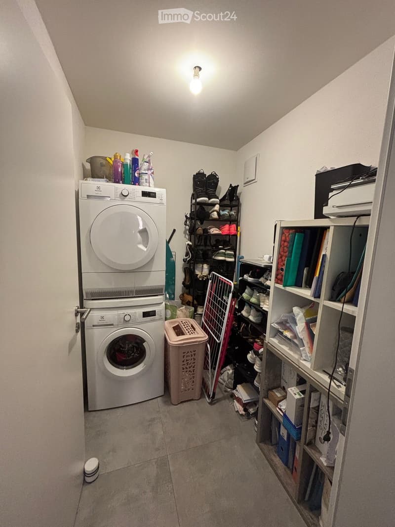 Laundry room with a washing machine, dryer, shelves filled with shoes and cleaning supplies, and a laundry basket.