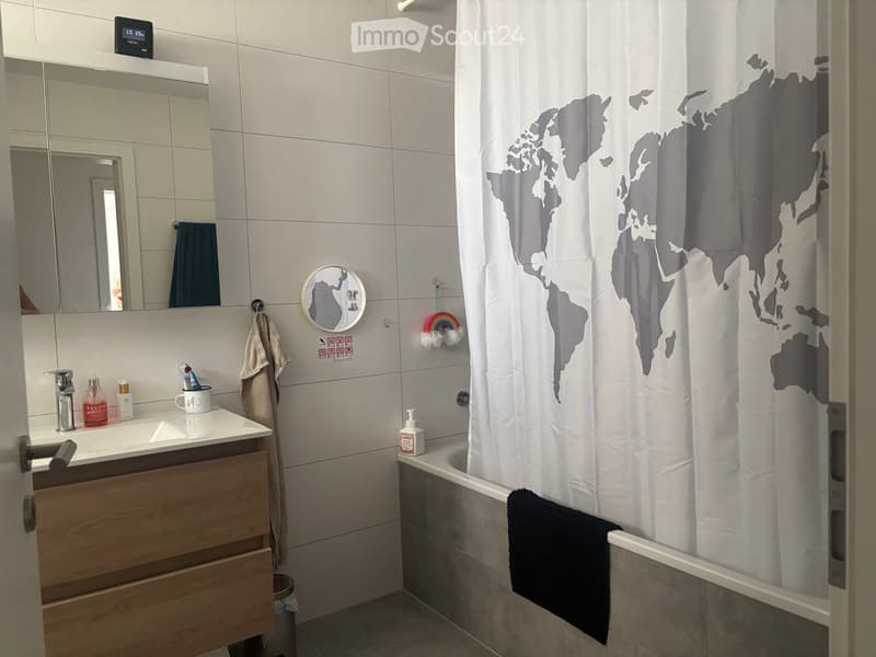 Modern bathroom with a white tiled wall, a wooden vanity with a sink, a mirror, and a bathtub with a world map shower curtain.