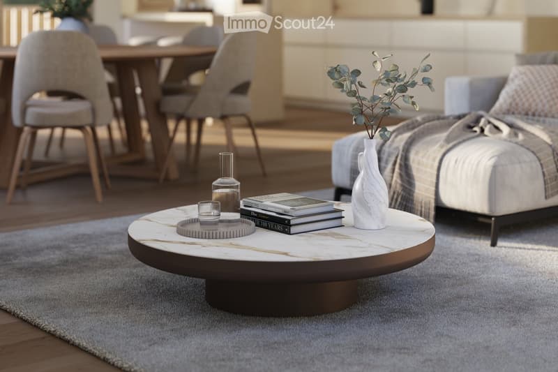 Modern living room with a grey sofa, a round marble coffee table, a vase with dried leaves, and a dining area with chairs and a table in the background.