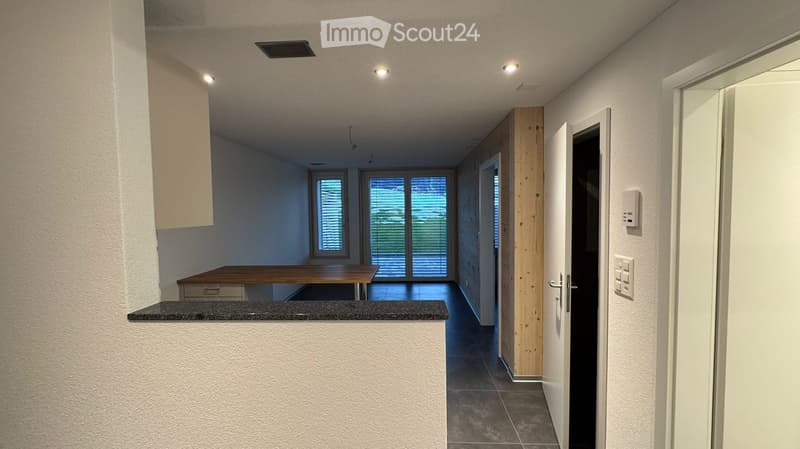 Empty room with wooden table, white walls, gray floor, wooden pillar, sliding glass doors, and a power outlet.