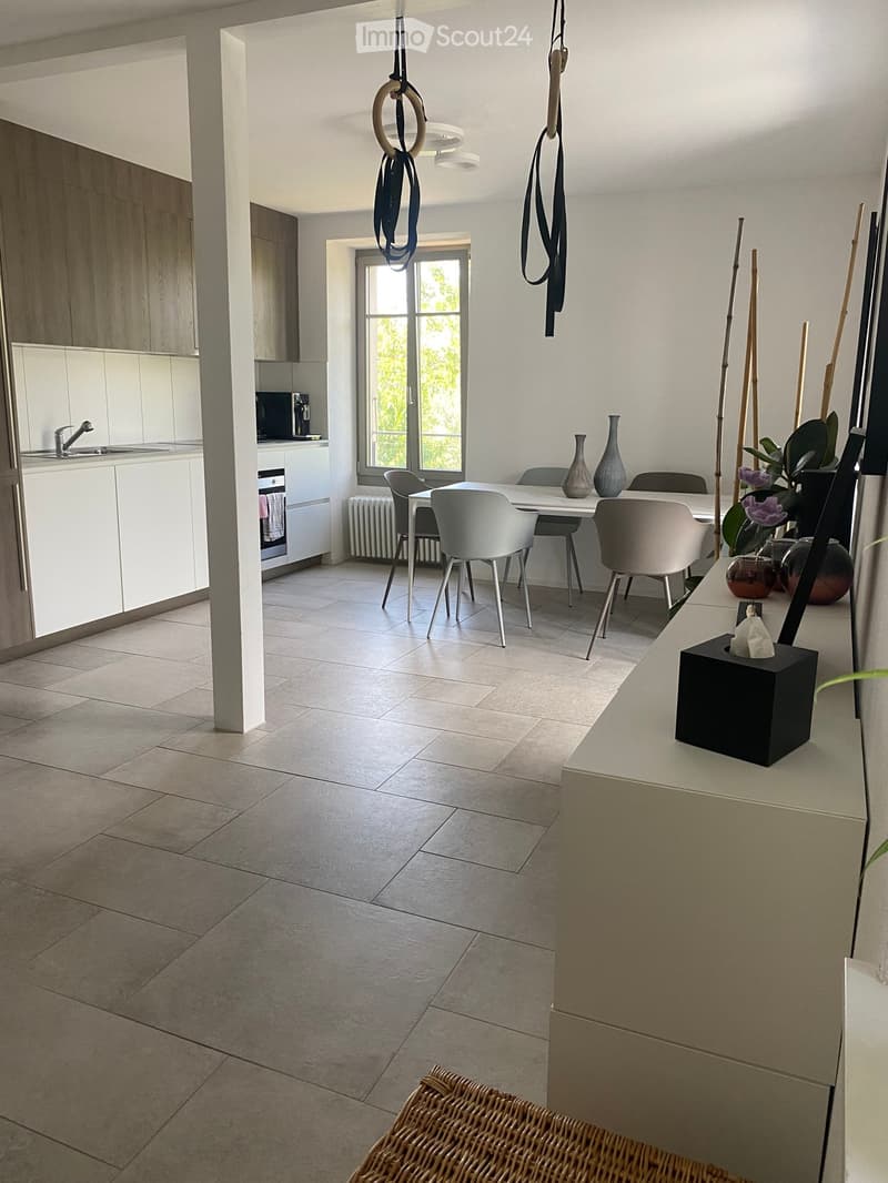 Modern kitchen and dining area with white cabinets, tiled floor, and a large window. Includes a sink, oven, dining table with chairs, decorative vases, and a plant on the counter.