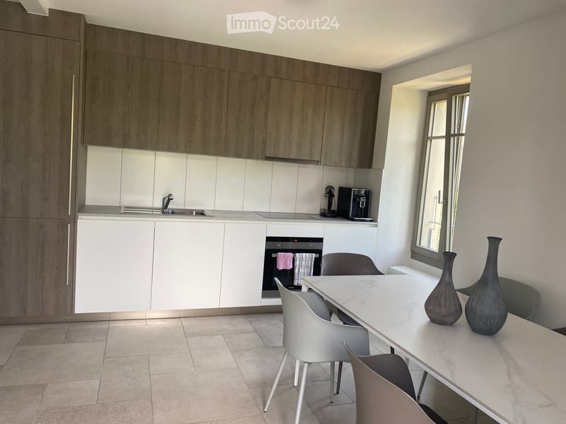 Modern kitchen with wooden cabinets, white countertops, stainless steel sink, built-in oven, and a dining area with a marble table and chairs.