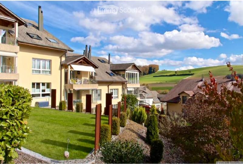 A multi-story residential house with a modern design, featuring large windows, balconies, and a well-maintained garden with neatly trimmed hedges and shrubs.
