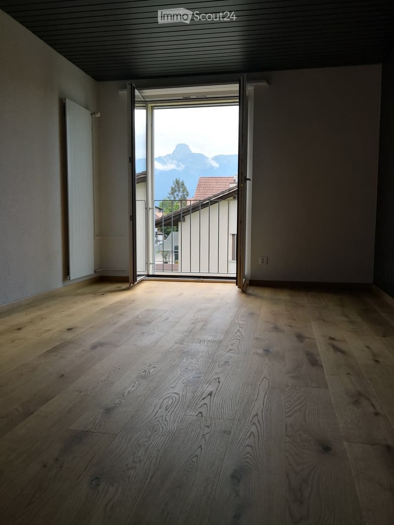 Empty room with wooden flooring, large open doorway leading to a balcony with a scenic mountain view.
