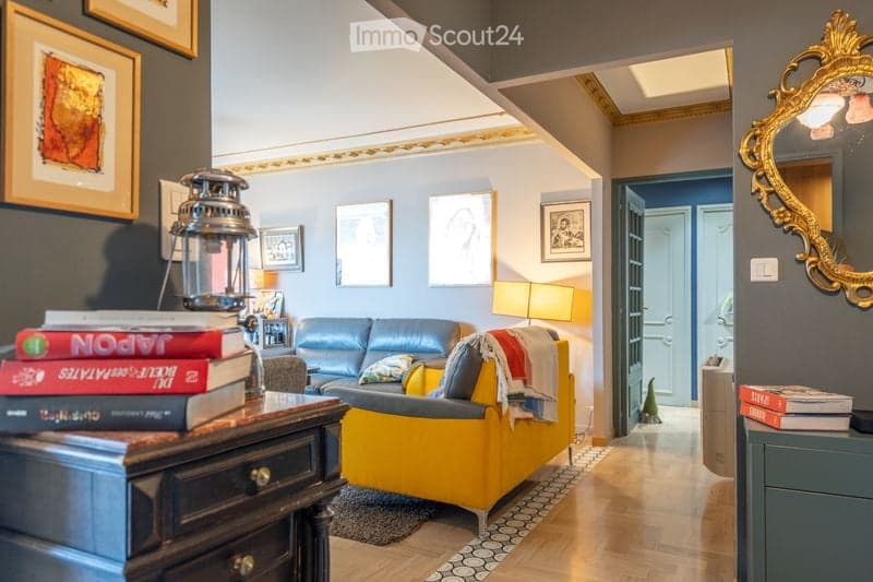 A cozy living room with a yellow armchair, blue sofa, wooden table with books, and a decorative mirror on the wall. The room features a warm, inviting atmosphere with a mix of modern and classic decor.