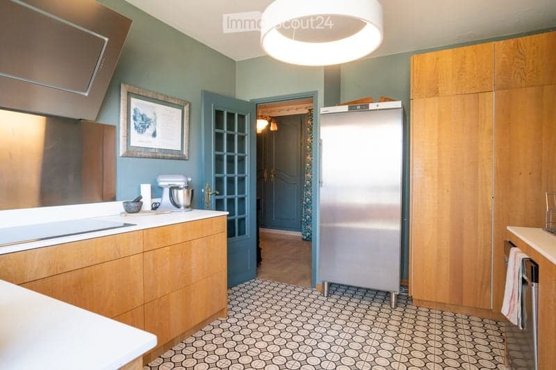 Modern kitchen with light wood cabinets, stainless steel appliances, and a patterned tile floor. Features a mixer on the counter and a framed picture on the wall.