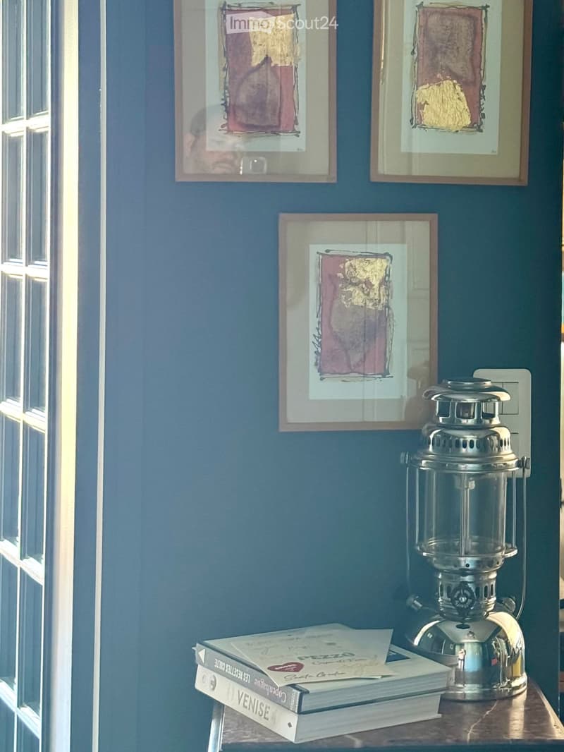 A small table with books and a lantern, against a blue wall with framed artwork.