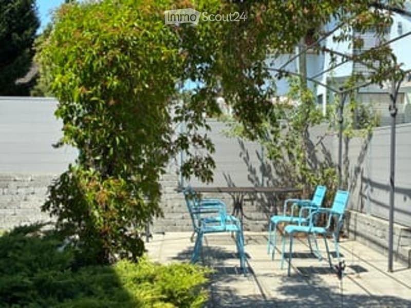 A small patio area with a table and four blue chairs, surrounded by greenery and a brick wall.