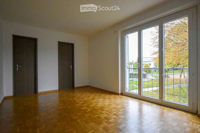 Empty room with wooden flooring, two doors, and large sliding glass doors leading to a balcony or outdoor area.