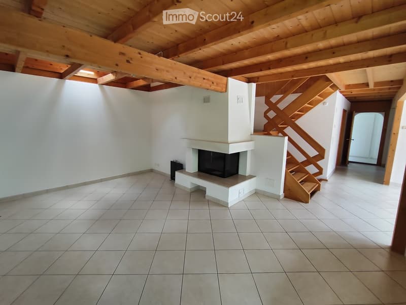 Empty room with exposed wooden beams, tiled floor, and a built-in fireplace. A wooden staircase leads to an upper level.