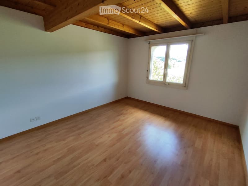 Empty room with wooden flooring, white walls, and a window with white frame. Exposed wooden beams on the ceiling.