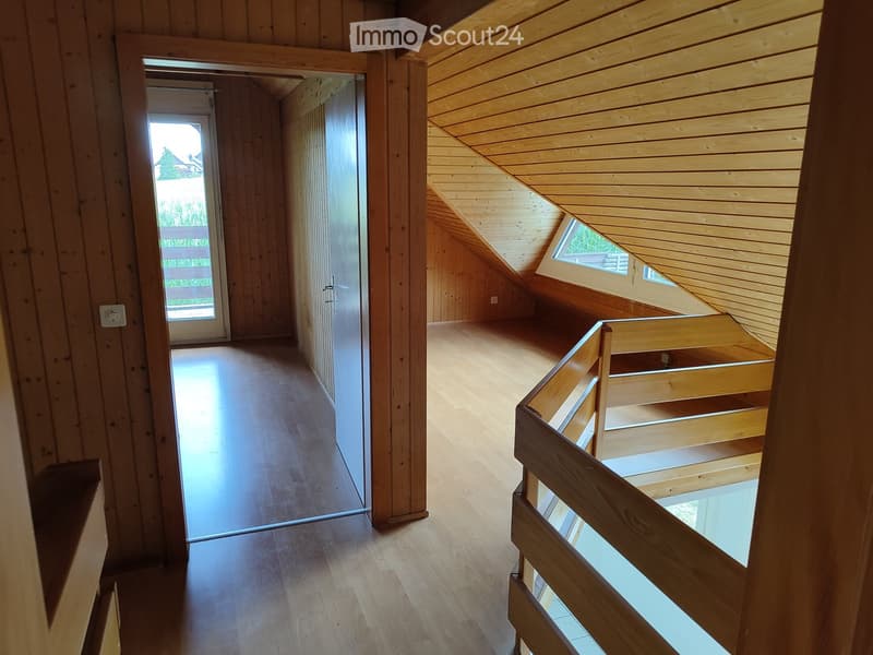 Empty attic space with wooden walls, floor, and ceiling, featuring a staircase leading to a lower level and a door to the outside.