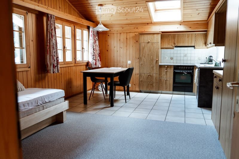 A cozy, wooden-paneled room with a bed, a dining table with chairs, and a kitchen area featuring cabinets, an oven, and a sink.