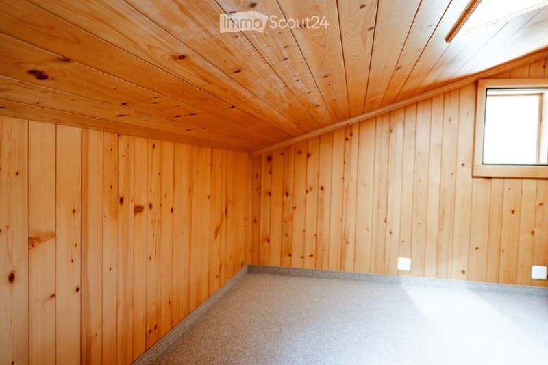 Completely empty room with wooden walls and ceiling, grey floor, and a small window on one wall.