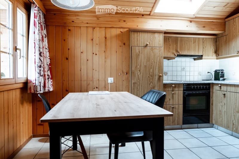 Cozy kitchen with wooden walls and cabinets, a dining table with chairs, and an oven.