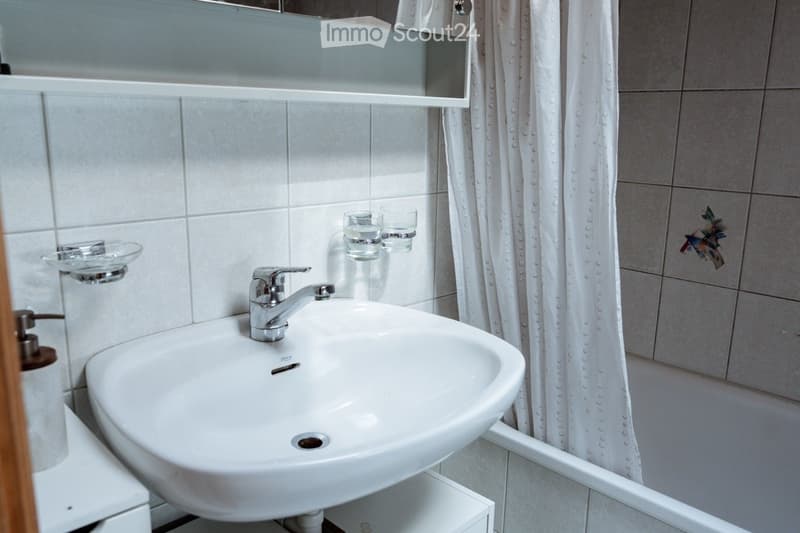 Bathroom with a white sink, chrome faucet, mirror, shower curtain, soap dispenser, and two cups on the wall.