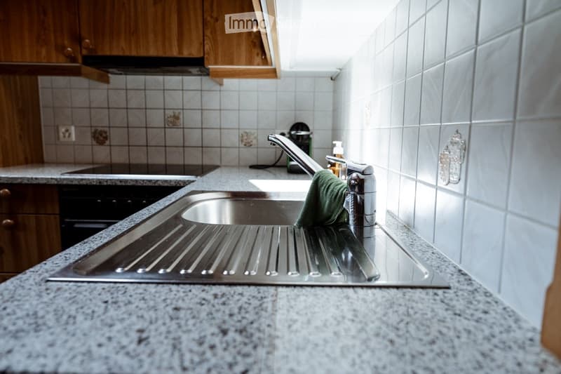 Modern kitchen with granite countertops, stainless steel sink, wooden cabinets, and a green towel draped over the faucet.