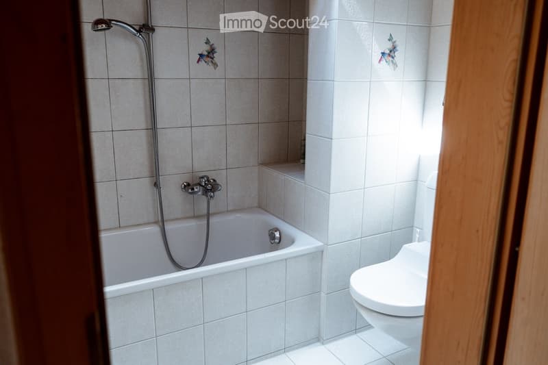 Bathroom with a bathtub, toilet, tiled walls, and a showerhead attached to the wall.