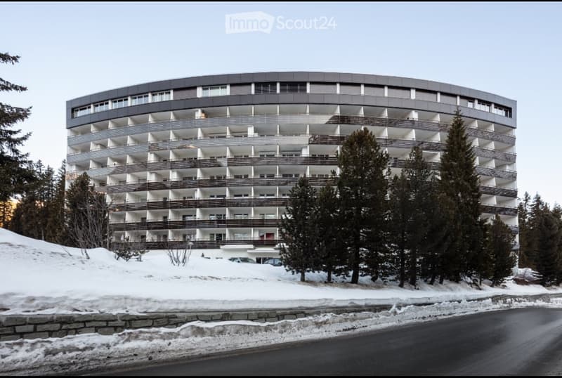 A modern architectural building with many windows and balconies on a snowy hill.