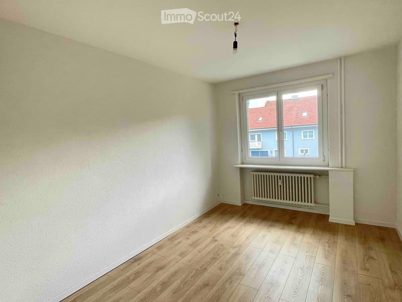 Empty room with wooden flooring, light-colored walls, a window with a radiator below, and a single ceiling light fixture.