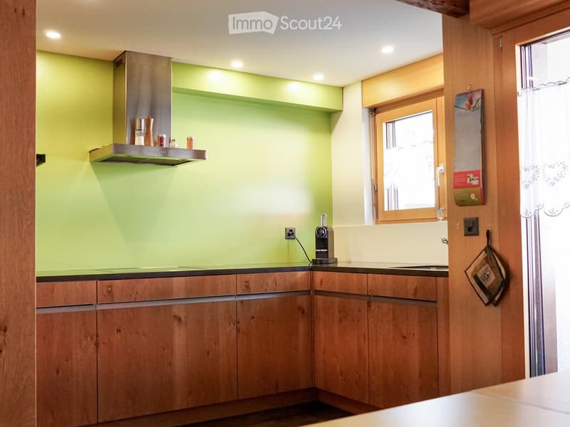 Modern kitchen with wooden cabinets, stainless steel range hood, coffee maker, and a window with a view.