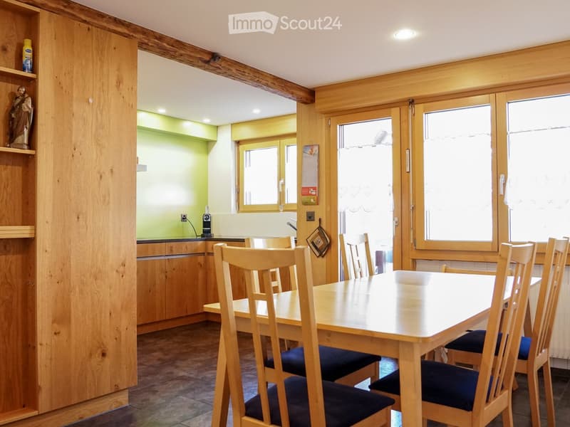 A cozy dining area with a wooden table and chairs, a kitchen area with cabinets and a sink, and wooden walls and beams.