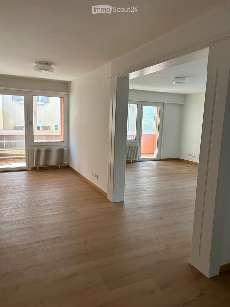 Empty room with wooden flooring, white walls, and large windows leading to a balcony area.