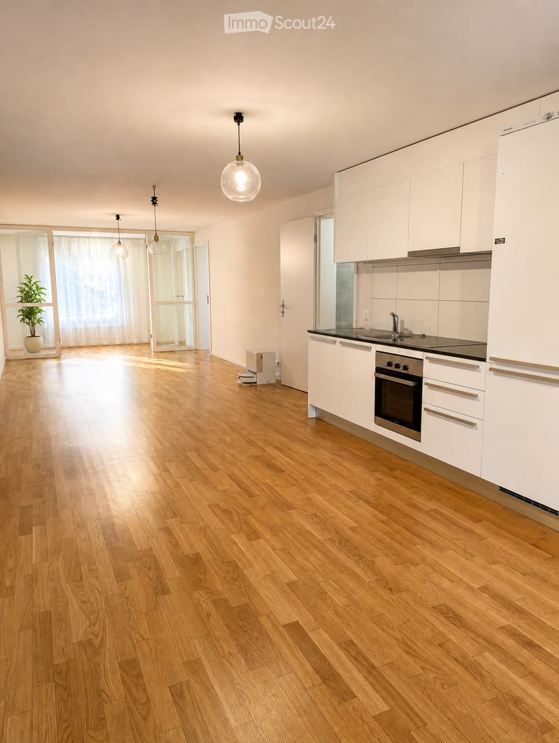 Modern kitchen with white cabinets, wooden flooring, and pendant lights. Features a refrigerator, oven, and sink.