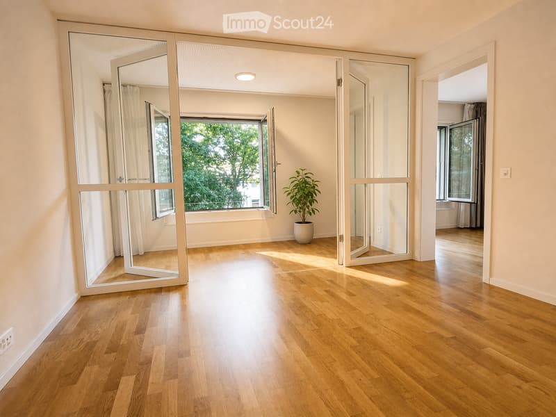 Empty room with wooden flooring, large windows, and a potted plant in the corner.