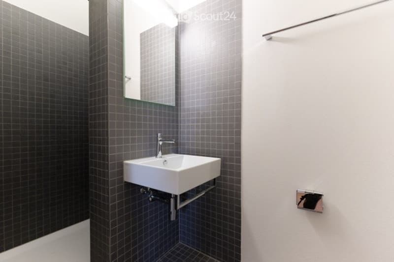 Modern bathroom with dark grey tiled walls and floor, white sink, and a large mirror above it.