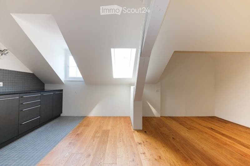 Bright, open attic space with wooden flooring, exposed beams, and skylights. Features built-in kitchen cabinets and drawers along one wall.
