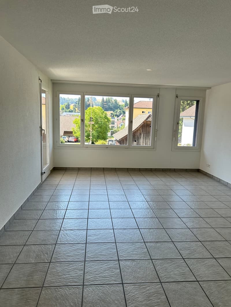 Empty room with tiled floor and large windows offering a view of the neighborhood.