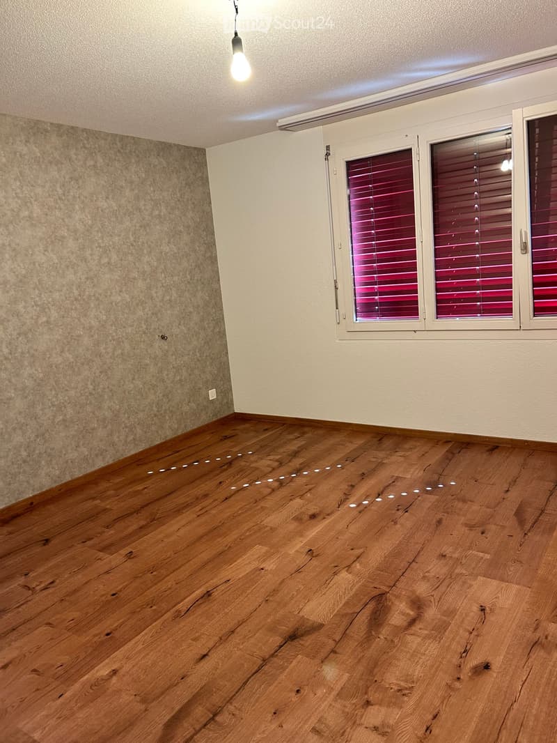 Empty room with wooden flooring, white walls, and large windows with blinds. No furniture or equipment present.