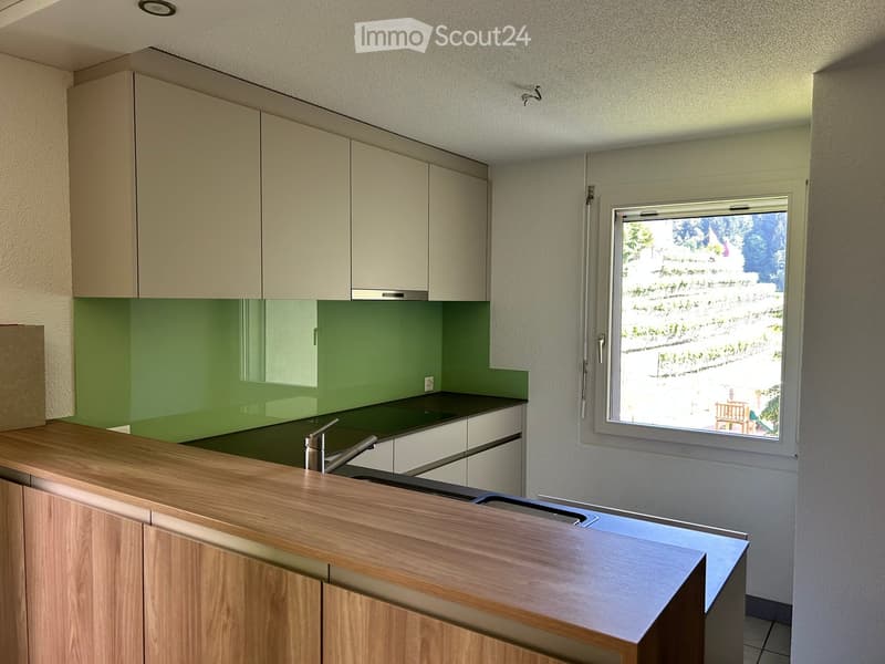 Modern kitchen with light-colored cabinets, green backsplash, wooden countertop, and stainless steel sink.