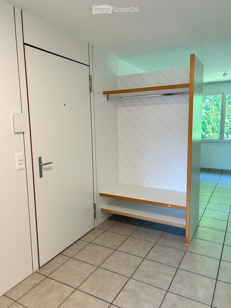Empty room with tiled floor, white walls, built-in wooden shelving unit, and a door with a silver handle.