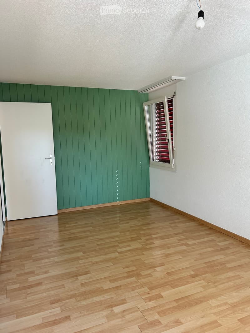 Empty room with wooden flooring, green paneled wall, white door, and window with blinds.