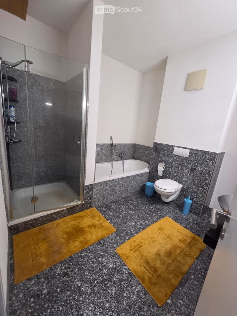 Modern bathroom with a bathtub, toilet, shower, and two yellow towels on the floor.
