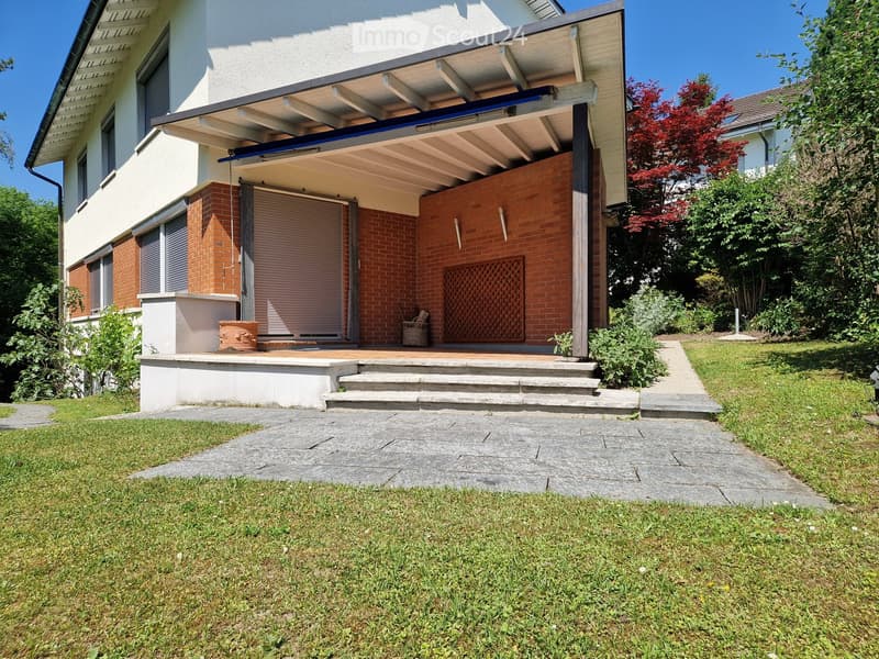 Front yard with a covered patio area, steps leading up to the house, and surrounding greenery.