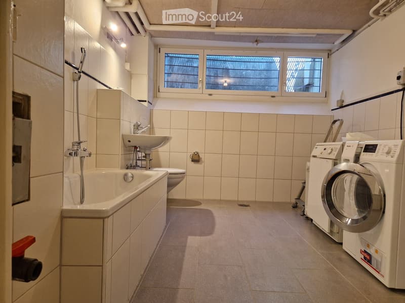 Bathroom with bathtub, toilet, sink, and washing machine. Features tiled walls and floor, with a window above the sink.