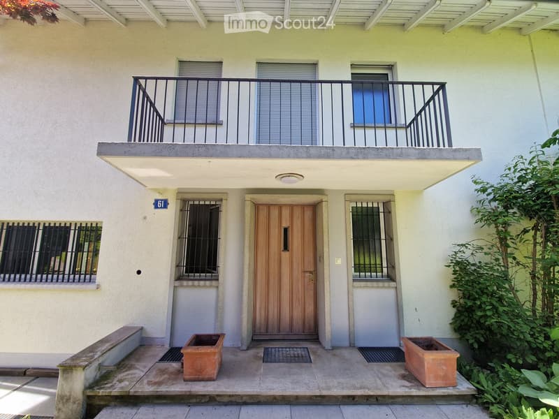 Two-story building with a raised ground floor, featuring a wooden front door, windows with metal bars, and a balcony above.